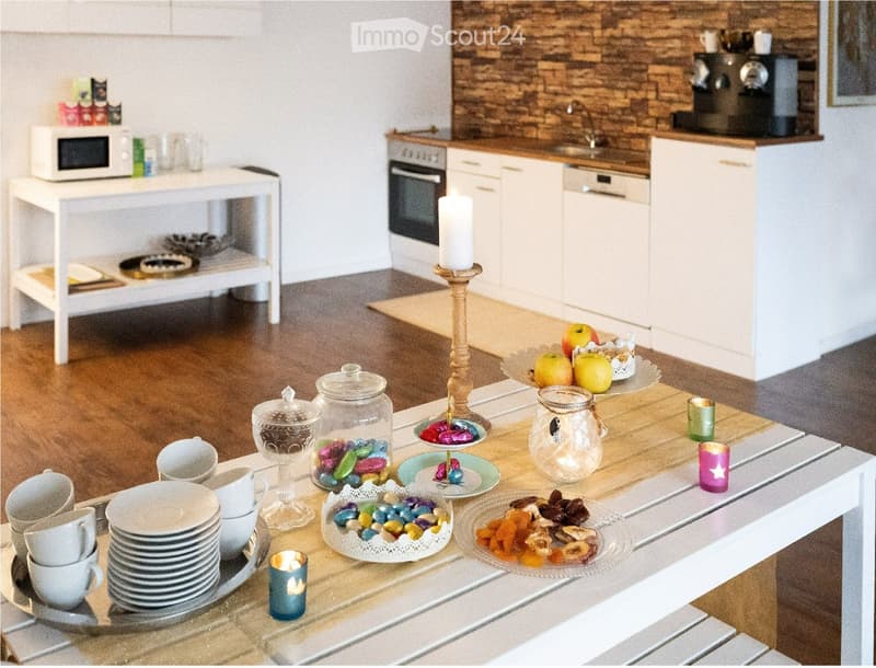 A modern kitchen with white cabinets, a wooden countertop, and a dining table set with plates, cups, and decorative items.