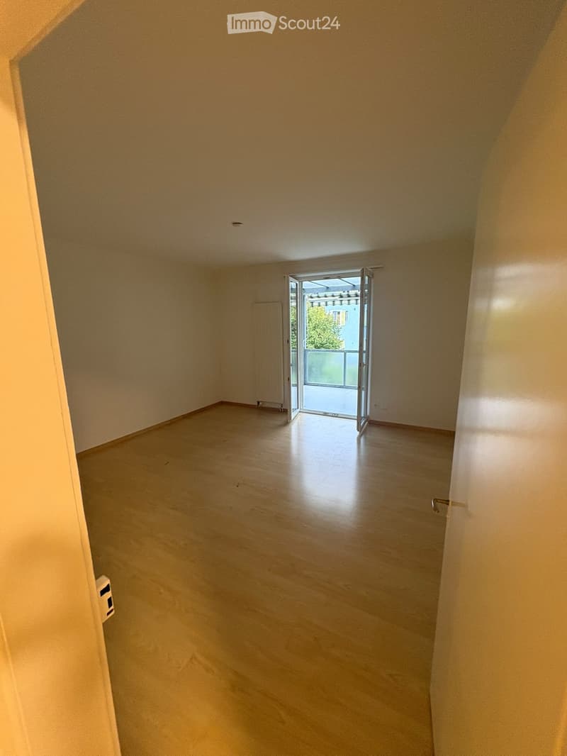 Empty room with light wooden flooring and white walls, featuring an open sliding door leading to a balcony area.