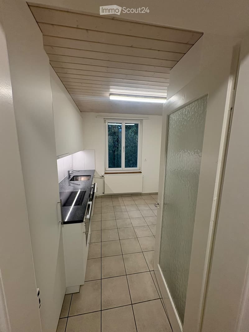Modern kitchen with white cabinets, tiled floor, stainless steel sink, and stove. Features a large window and a frosted glass door leading to another room.
