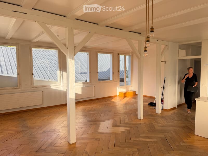 Empty room with wooden flooring, white walls, large windows, and exposed wooden beams on the ceiling. No furniture or equipment is present.