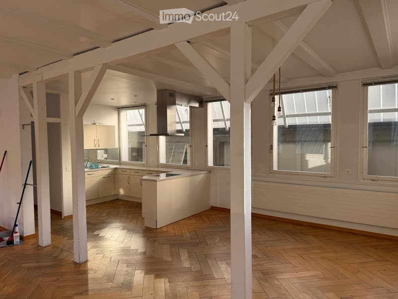 Bright, open kitchen with wooden flooring, white cabinets, a central island, and large windows allowing natural light to fill the space.