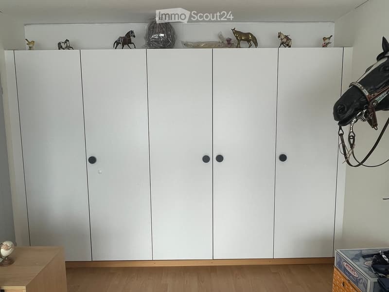 A room with a large white wardrobe, several toy horses on top, and a small globe on a wooden stand.