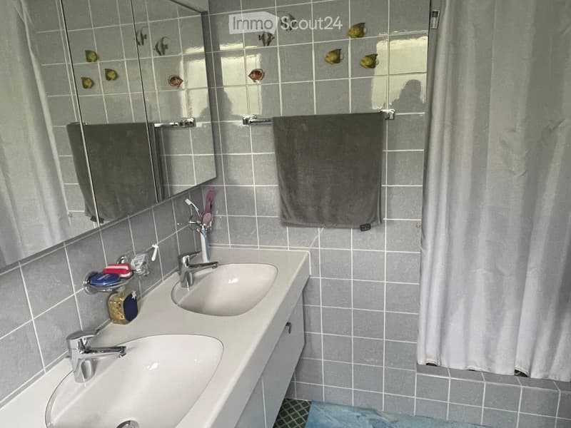A modern bathroom with two sinks, a large mirror, a towel hanging on a rack, and a shower curtain partially visible.