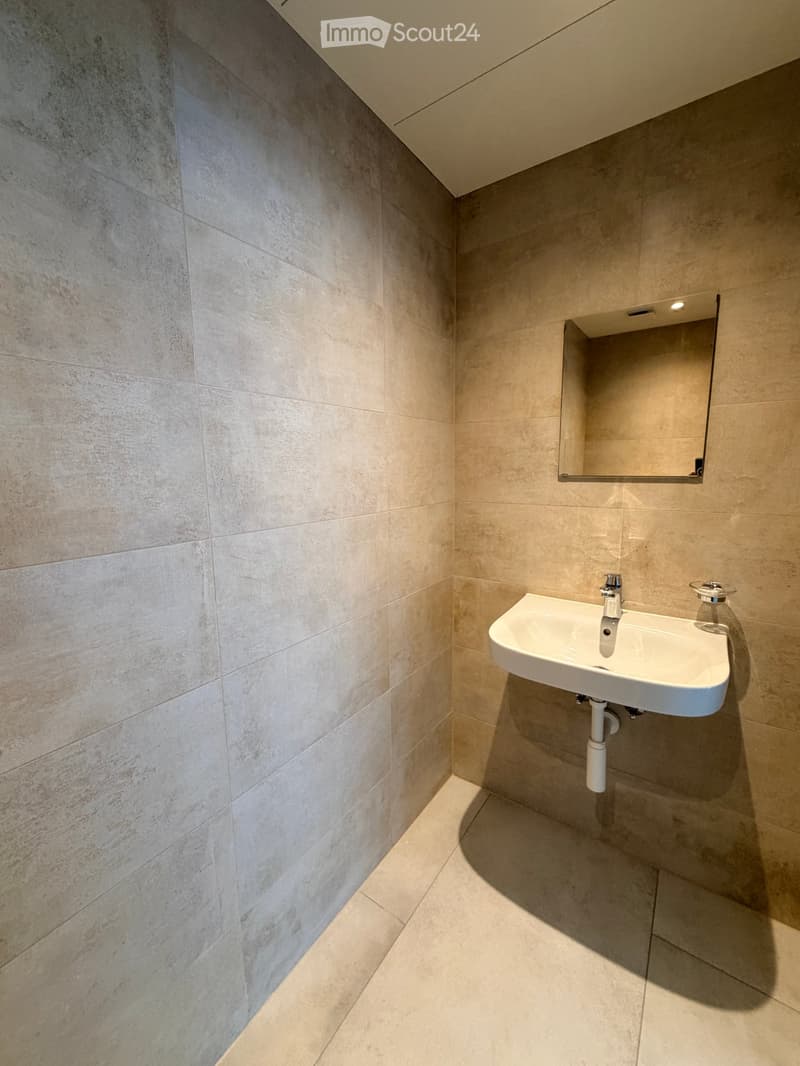 Modern bathroom with a white sink, chrome faucet, and a built-in mirror above it. The walls and floor are covered in light beige tiles.