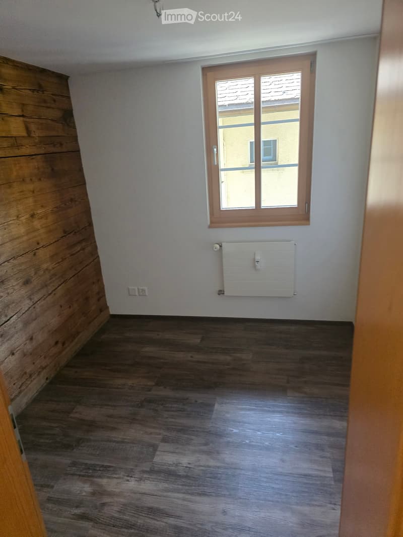 Empty room with wooden flooring, white walls, a window with wooden frame, and a radiator below it.