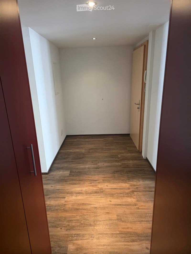 Empty hallway with wooden flooring, white walls, and recessed lighting. Features a closed door on the right and an open door on the left.