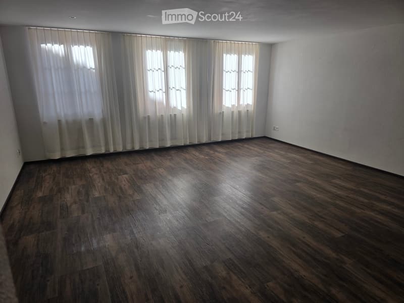 Empty room with wooden flooring and large windows covered by white curtains. No furniture or equipment present.