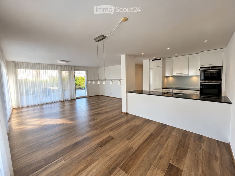 Modern kitchen with white cabinets, black countertop, pendant light, and large window with curtains leading to a balcony.