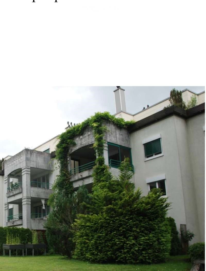 Modern multi-story building with green ivy covering the facade, multiple balconies, and surrounding greenery.