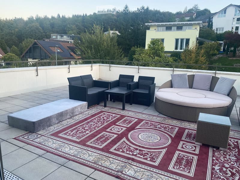 Balcony with a round sofa, chairs, a coffee table, and a patterned rug on a tiled floor.