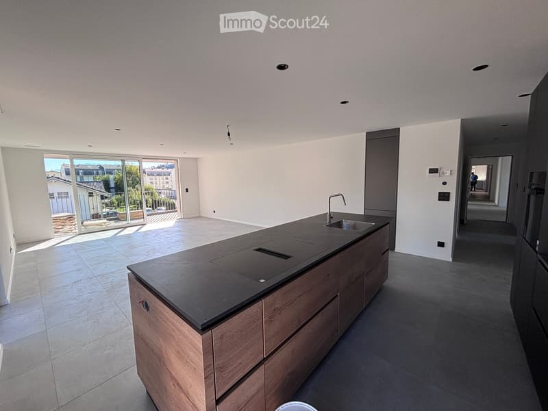 Modern kitchen with a central island, dark countertop, and built-in sink. Large windows provide natural light and a view of the outdoor area.