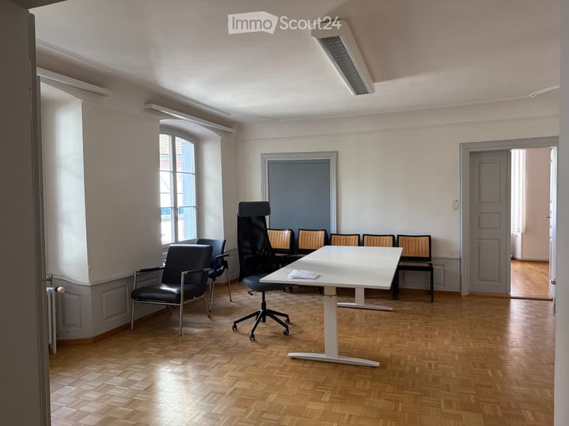 Office space with wooden flooring, white table, and several black chairs arranged around it.