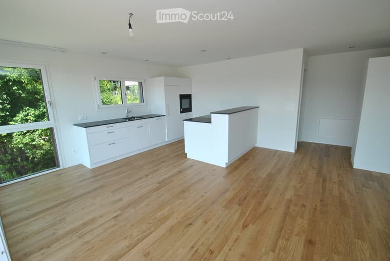 Modern kitchen with white cabinets, wooden flooring, and a central island. Features a sink, oven, and ample natural light from large windows.