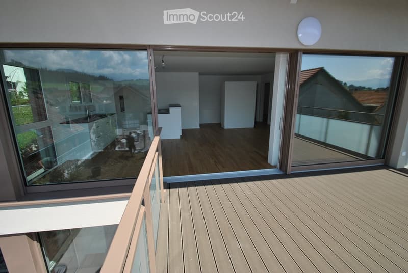 Modern balcony with wooden decking, large glass sliding doors leading to an interior space, and a view of the surrounding landscape.
