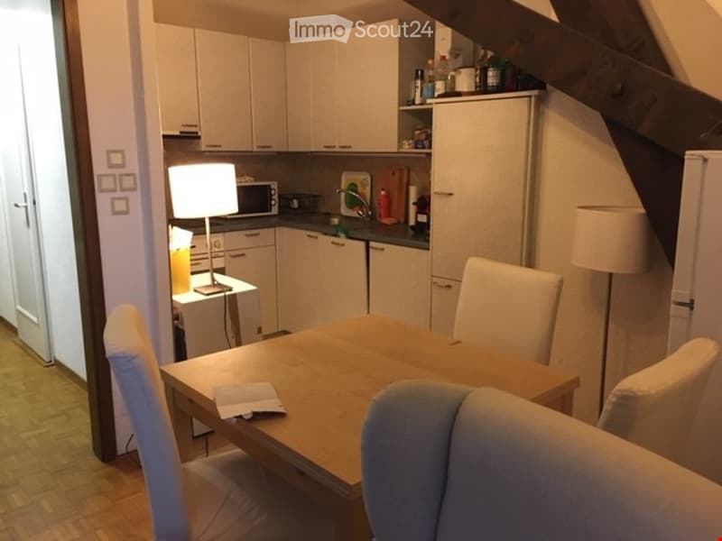 Modern kitchen with white cabinets, a dining table with chairs, a refrigerator, microwave, and a lamp on a side table.