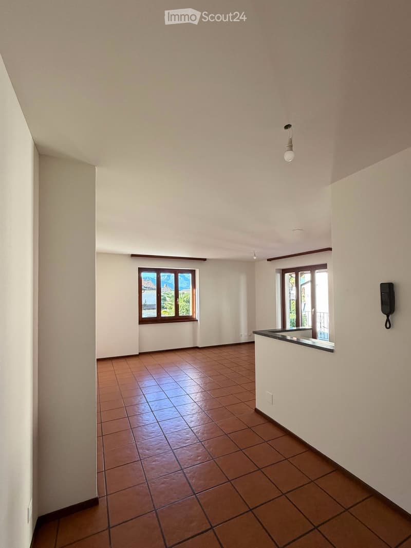 Empty room with tiled floor, white walls, and two windows offering a scenic view. There is a small black countertop on the right side.