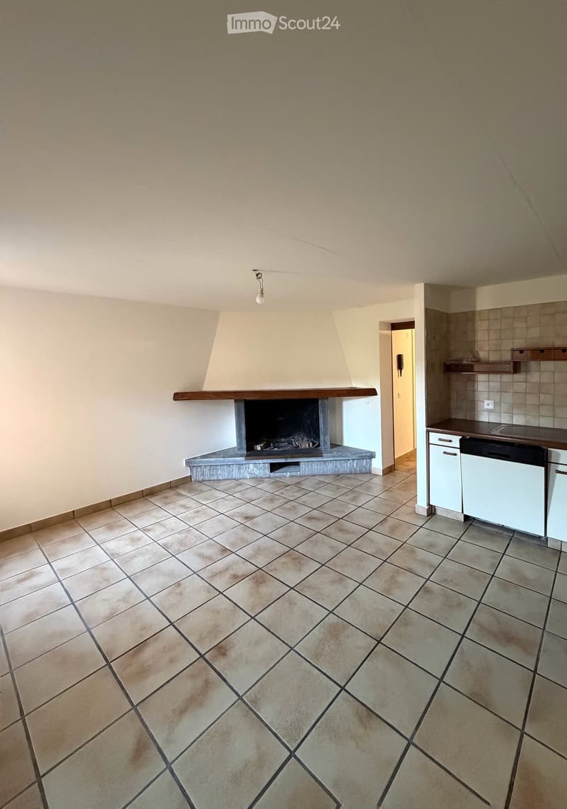 Open-plan living and kitchen area with tiled flooring, a fireplace, and a small kitchen section featuring cabinets and a sink.