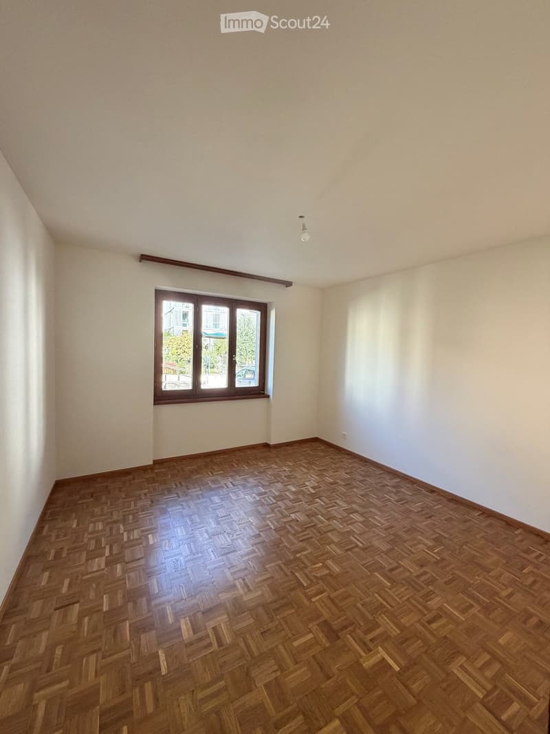 Empty room with wooden herringbone flooring, white walls, and a single window with wooden frame and glass panes.