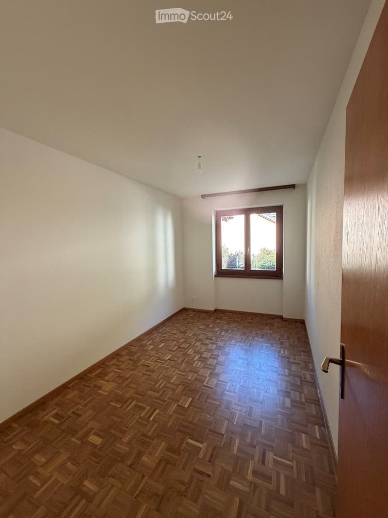 Empty room with wooden herringbone flooring, white walls, and a single window with wooden frame. No furniture or equipment present.