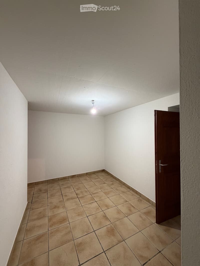 Empty room with tiled floor and white walls, featuring a single door and a ceiling light fixture.