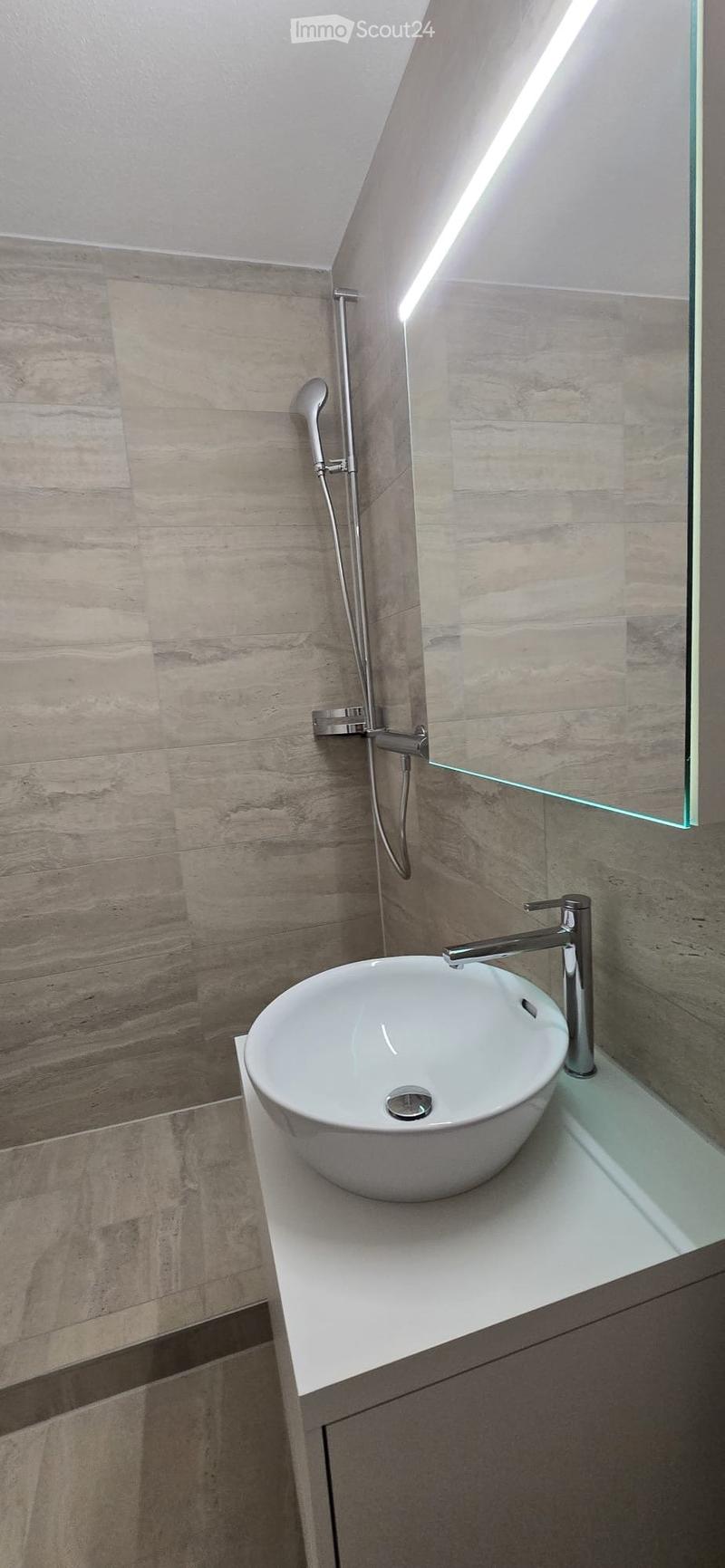 Modern bathroom with a white sink, sleek faucet, glass mirror, and a modern showerhead mounted on the wall.