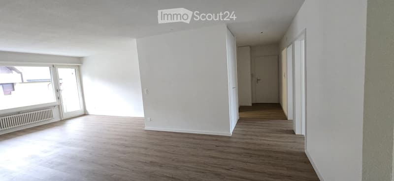 Empty room with wooden flooring, white walls, large window with sliding doors, and a radiator below the window. No furniture or equipment present.