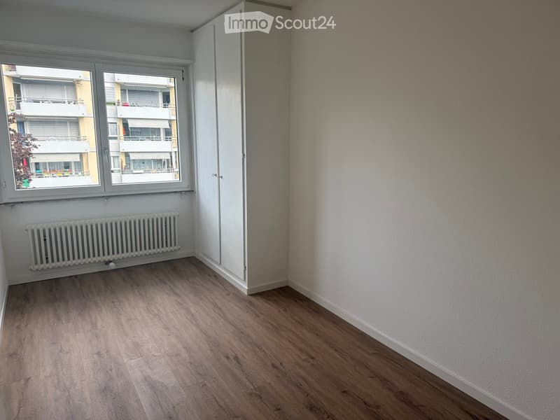 Empty room with wooden flooring, white walls, a window with blinds, and a radiator under the window.