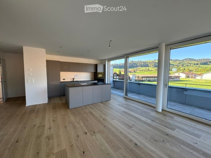 Modern kitchen with light grey cabinets, a central island, and large windows offering a scenic view of the countryside.