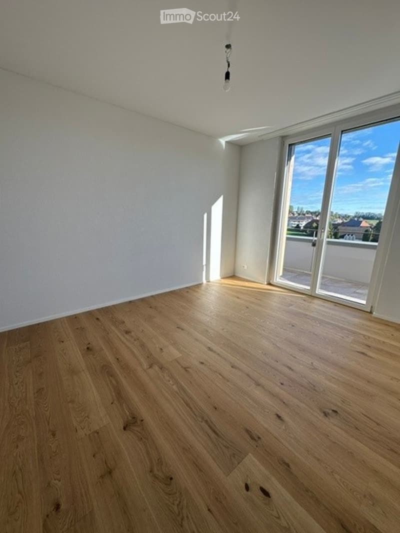Empty room with light wooden flooring, white walls, large windows, and a view of the outside.