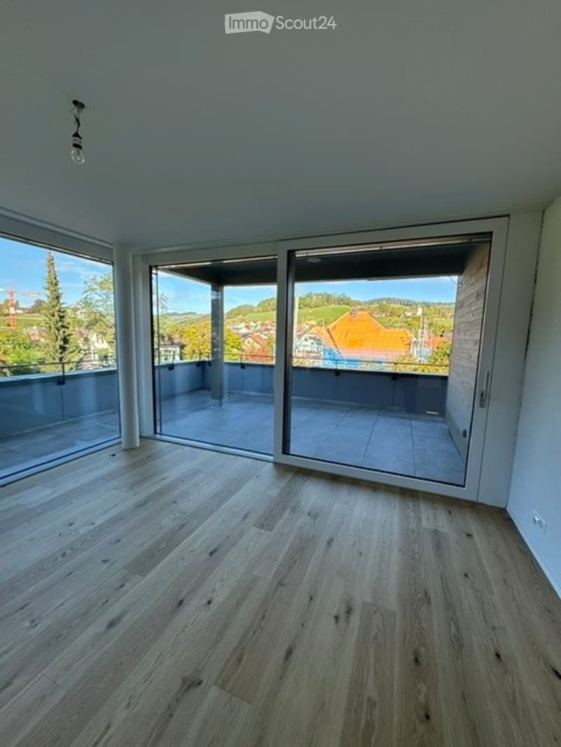 Bright, empty room with large sliding glass doors opening to a balcony, wooden flooring, and white walls.