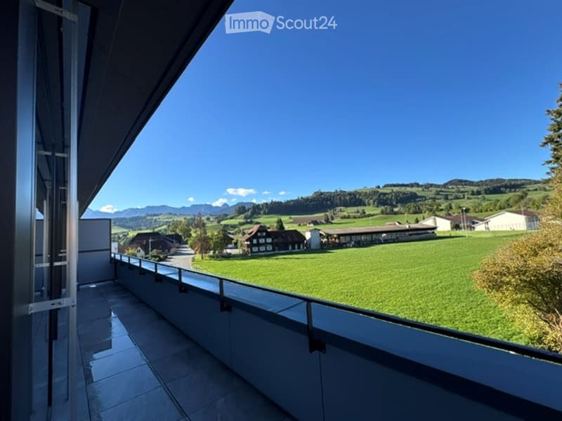 Balcony with a scenic view of a green field, distant mountains, and a small village.