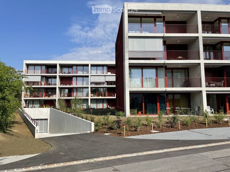 Modern two-story residential building with large windows, balconies, and a raised ground floor entrance.