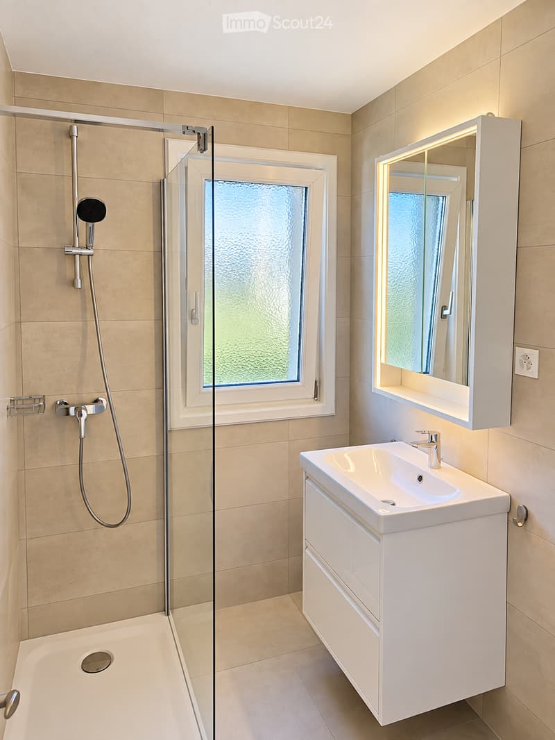 Modern bathroom with a white sink, mirror cabinet, glass-enclosed shower, and beige tiles.