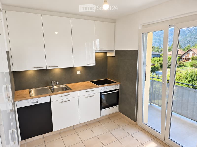 Modern kitchen with white cabinets, wooden countertop, stainless steel sink, oven, and dishwasher. Large window offers a scenic mountain view.