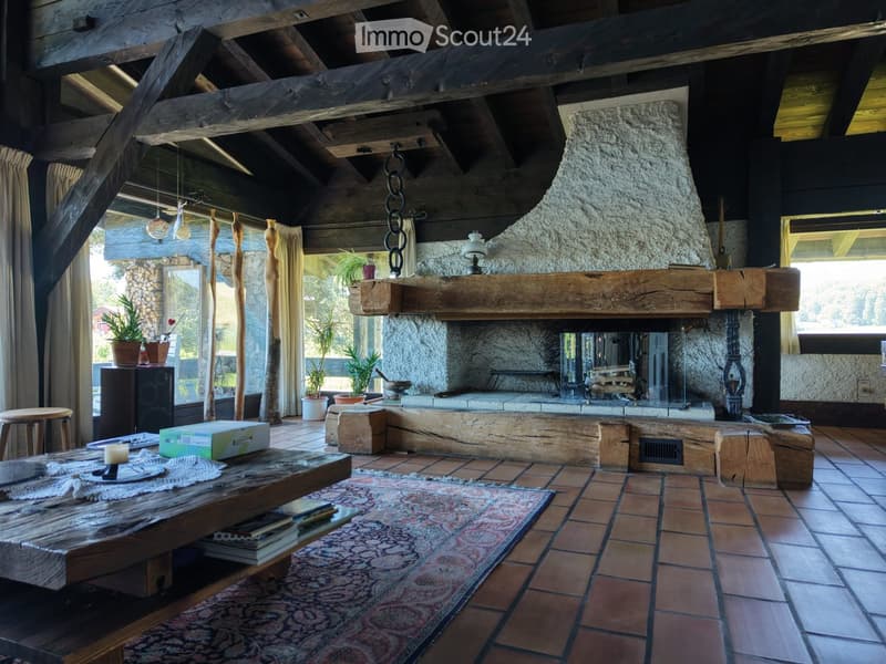 Living room with exposed wooden beams, stone fireplace, wooden table, and decorative items.
