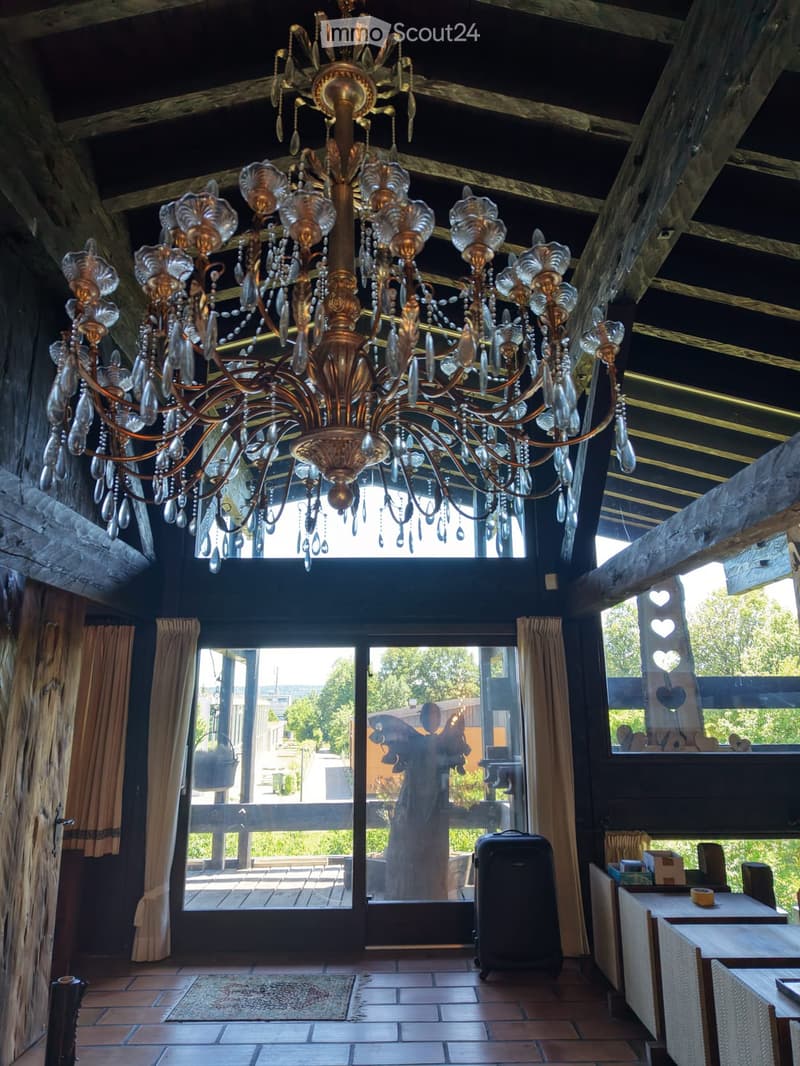 A room with a large, ornate chandelier, tiled floor, large windows with curtains, and a table with chairs.