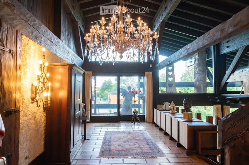 Elegant hallway with wooden beams, chandelier, large windows, and decorative items including a table with a sculpture and a candle holder.