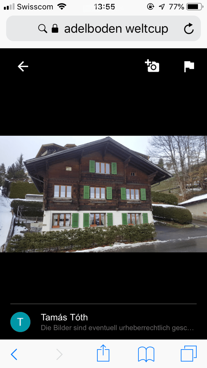 Traditional wooden house with green shutters and multiple windows, surrounded by snow-covered ground and trees.