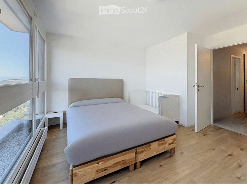 Modern bedroom with a wooden bed, nightstand, and large window offering a scenic view.