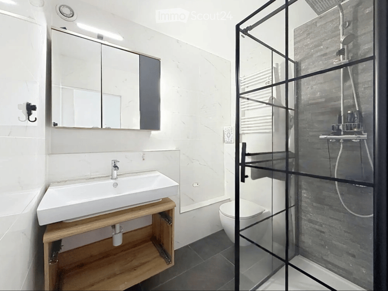 Modern bathroom with a white sink on a wooden stand, a large mirror, a toilet, and a glass-enclosed shower with a modern showerhead.