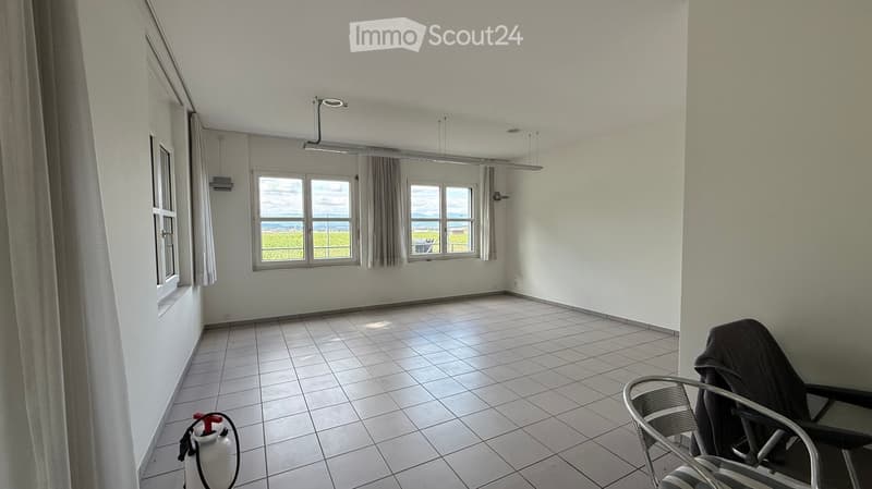 Empty room with white tiled floor, large windows with grey curtains, and a fire extinguisher in the corner.