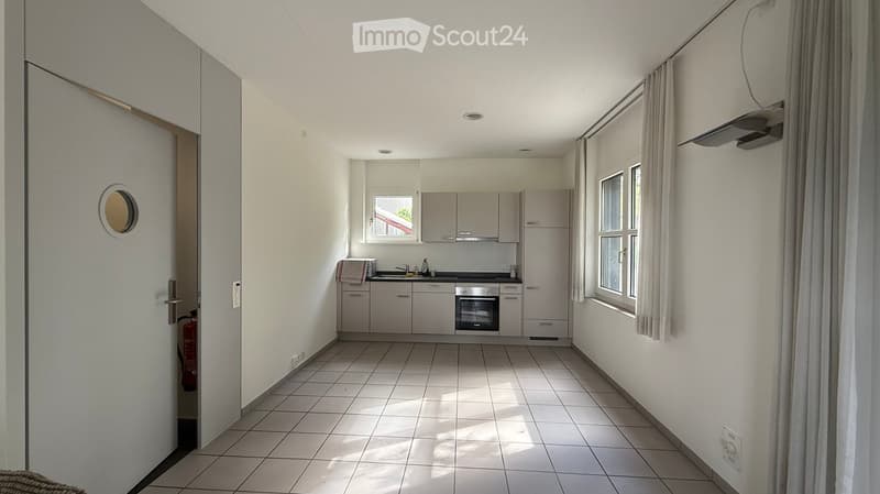 Modern kitchen with white cabinets, tiled floor, and stainless steel appliances including a sink, oven, and microwave. Natural light from windows illuminates the space.