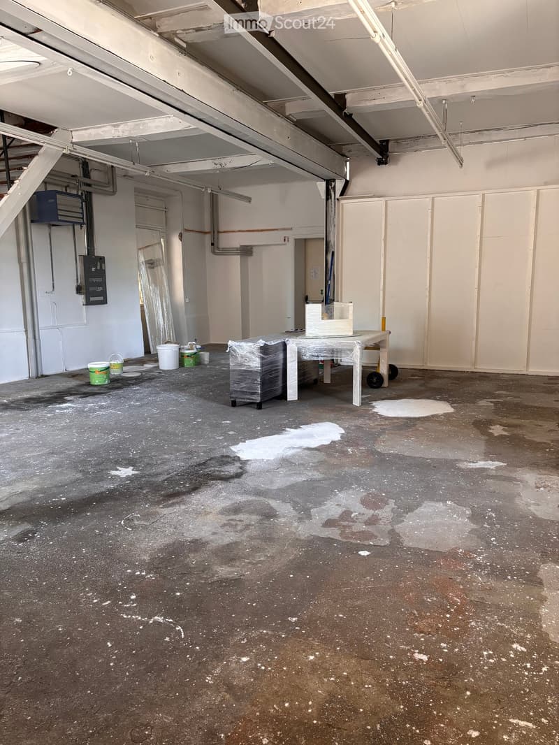 Empty room with bare walls, concrete floor, and minimal fixtures. Includes a small table, buckets, and a plastic container.