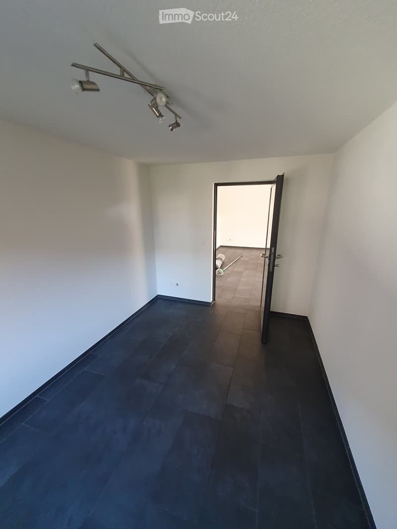 Empty room with dark tiled floor and light blue walls, featuring a ceiling light fixture and an open doorway leading to another room.