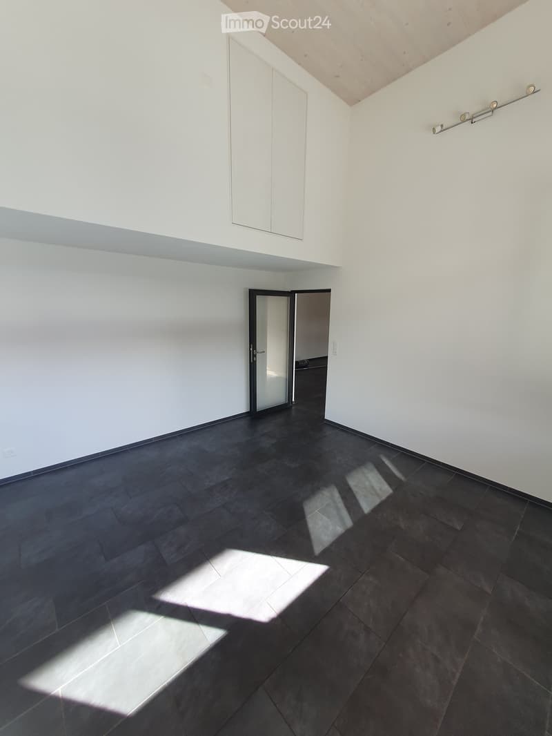 Empty room with dark tiled floor and white walls, featuring a large window and a door leading to another space.