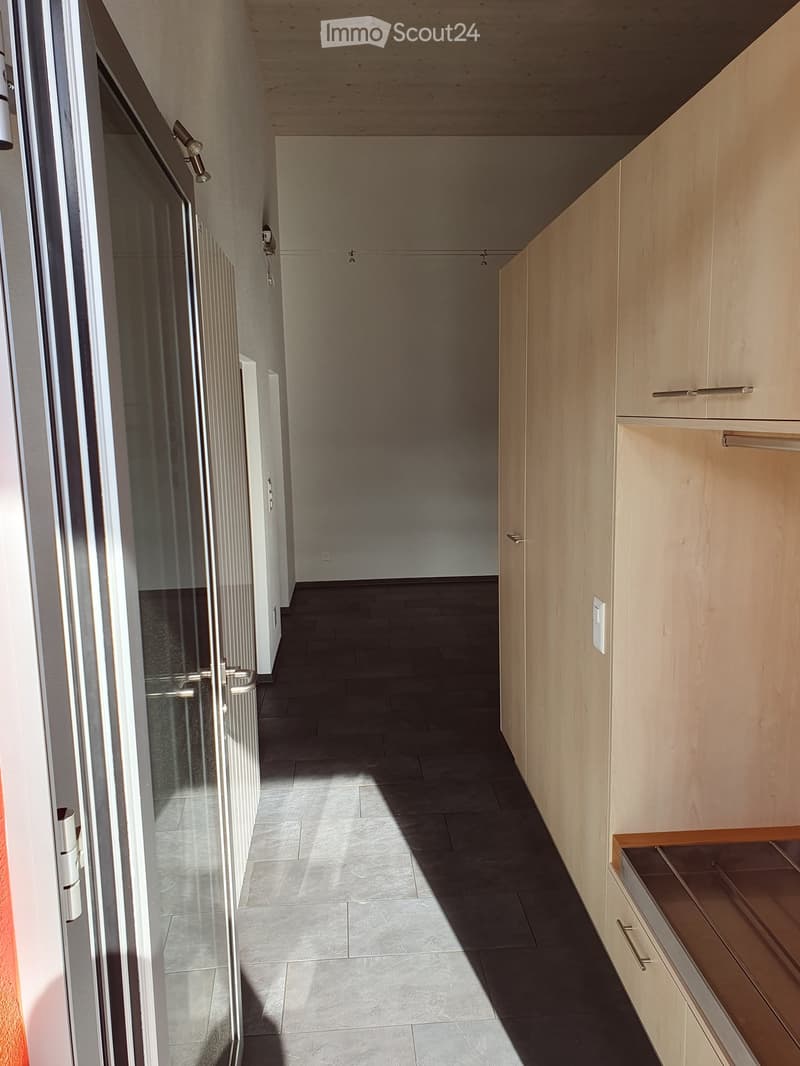 Empty hallway with tiled floor, light-colored walls, and built-in wooden cabinetry on one side.