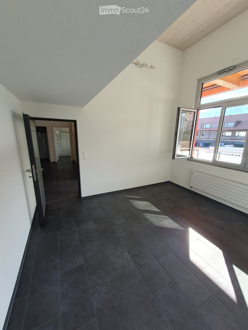 Empty room with dark tiled floor, white walls, large window with open shutters, and a door leading to another room.