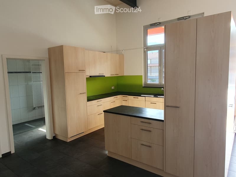 Modern kitchen with light wood cabinets, black countertop, and green backsplash. Features a window and a doorway leading to another room.