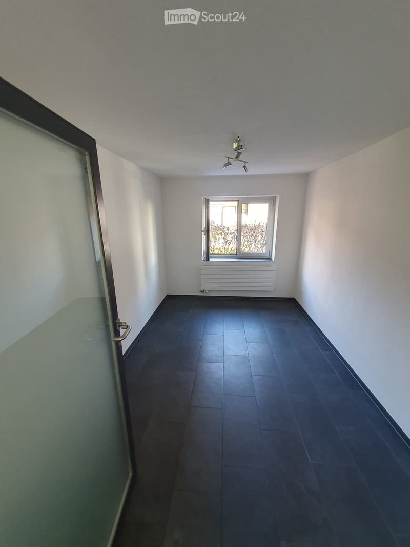 Empty room with dark tiled floor, white walls, a window with blinds, a radiator, and a ceiling light fixture.