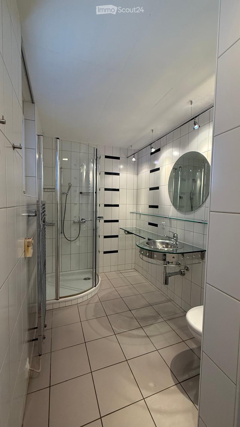 Modern bathroom with white tiles, a glass-enclosed shower, a sink with a mirror, and a toilet.